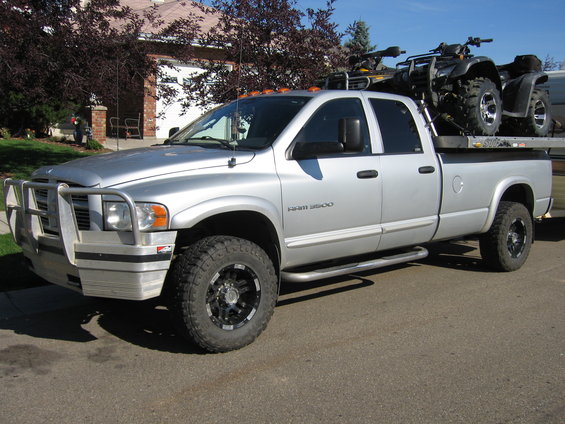 2005 Dodge 3500 pickup truck with bull bar, side steps, and two ATVs loaded in the flatbed
