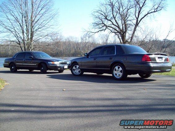 Two dark sedans, one 2003 Mercury Grand Marquis with alloy wheels and a spoiler, the other a similar model with black wheels, parked outdoors