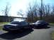 1999 Mercury Grand Marquis - Two dark sedans are parked on a paved path with trees and a body of water in the background.