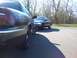1999 Mercury Grand Marquis - Two dark sedans, one a 1999 Mercury Grand Marquis, are parked side-by-side on an asphalt surface with trees in the background.