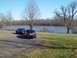 1999 Mercury Grand Marquis - Two sedans are parked on a paved area next to a body of water on a clear day.