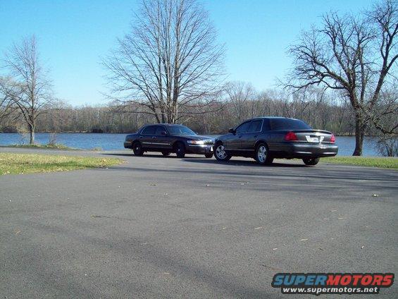 Two dark sedans parked by a lake, one slightly in front of the other