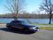 1999 Mercury Grand Marquis - A dark sedan is parked on the side of a road next to a lake on a clear day.