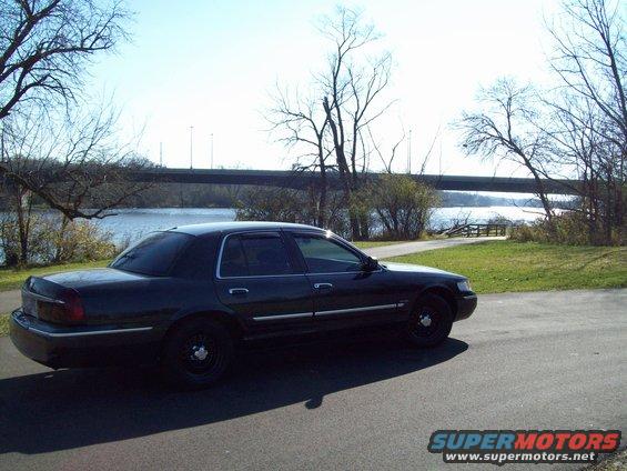 Dark sedan parked on asphalt near a body of water with a bridge in the background