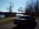 1999 Mercury Grand Marquis - A dark sedan is parked on a path next to a body of water with trees and a bridge visible.