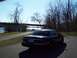 1999 Mercury Grand Marquis - A dark sedan is parked near a body of water with trees in the background.
