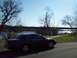 1999 Mercury Grand Marquis - A dark sedan is parked on a paved surface next to a grassy area with trees and a river.