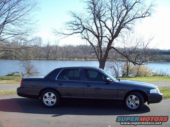 Dark sedan parked on asphalt near a body of water with trees in the background