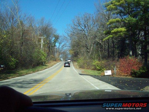 View from inside a car looking down a two-lane road with two other cars ahead