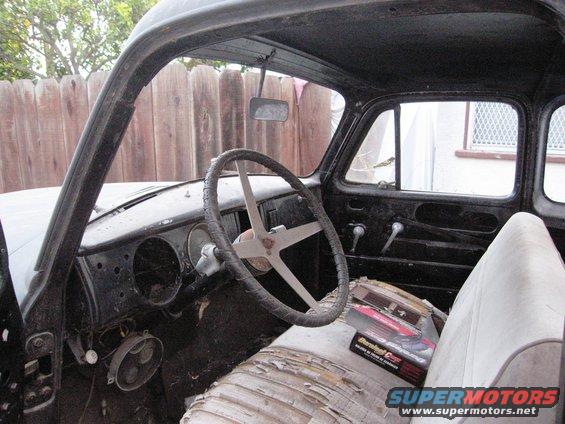 Interior of a vintage truck with a worn steering wheel and torn seat