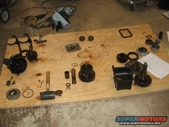 Disassembled transmission gears, bearings, and tools on a plywood sheet