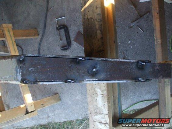 Welded steel beam with visible weld marks, clamped to wooden supports
