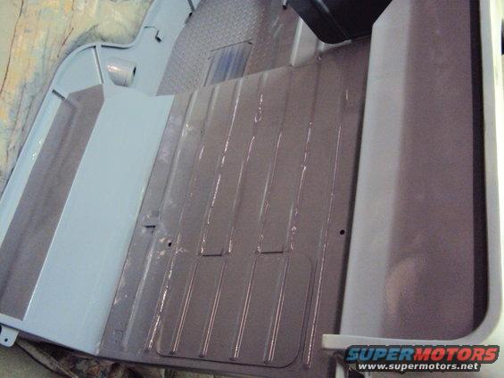 Gray painted metal floor of a vehicle, showing ribbed sections and a flat panel