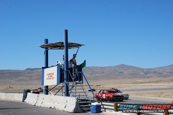 Race cars on a track with a scoring tower. One car is red with number 71