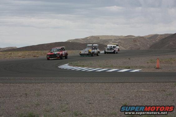 Three race cars on a track, one red, one gray, one white
