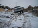 1989 Ford Bronco - A white Ford truck drives through a snowy, off-road terrain with rocky obstacles.