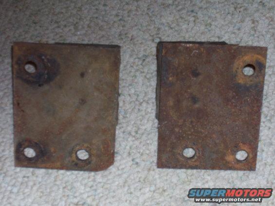 two rusty metal brackets with four holes each