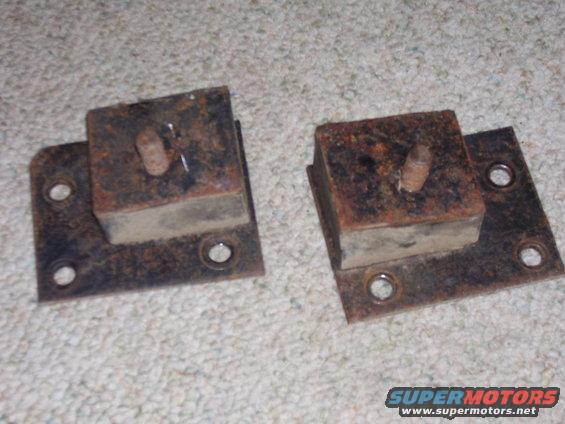 Two rusty metal brackets with rubber blocks and bolts, resting on carpet