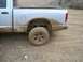 2005 Dodge 1500 - This silver pickup truck, likely a 2005 Dodge 1500, is seen from the rear side, heavily coated in mud from off-road use.