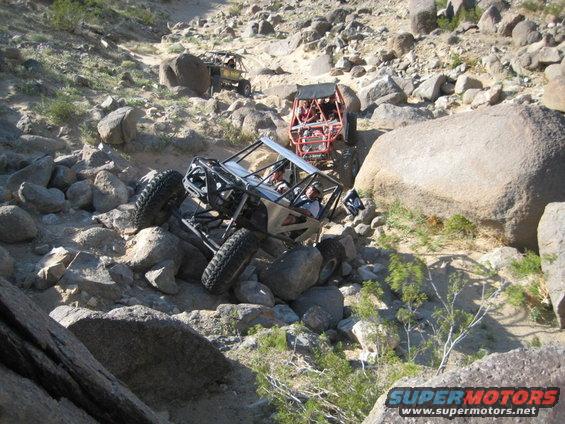 Silver off-road buggy climbing rocks, red buggy behind, yellow buggy in distance