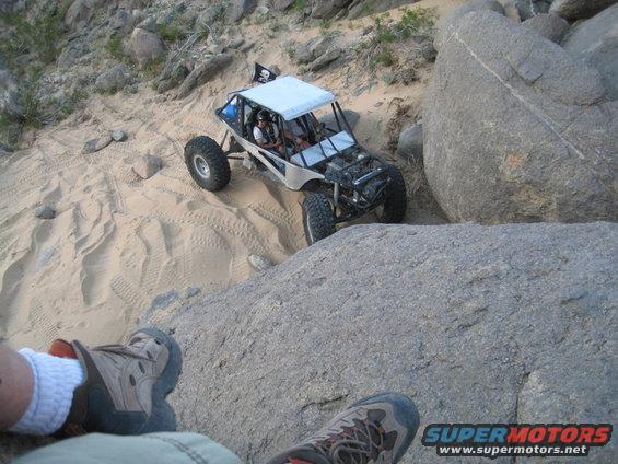 Off-road buggy climbing a sandy hill with large rocks around