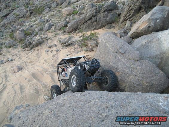 Custom off-road buggy with roll cage navigating large rocks on a sandy incline