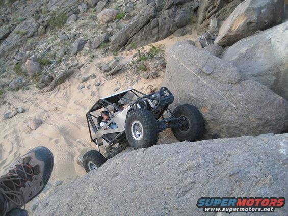 Off-road buggy with roll cage climbing a rocky incline, driver wearing helmet