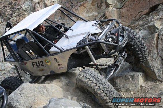 Off-road buggy with roll cage and large tires navigating rocky terrain. 'FU2' is visible on the side