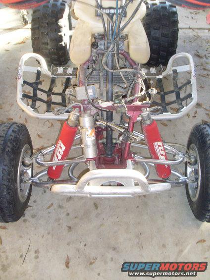 Front view of an ATV's suspension and engine area. Red shocks are visible