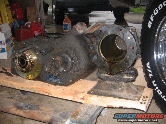Transfer case on wooden blocks, with a tire and part of a vehicle in the background