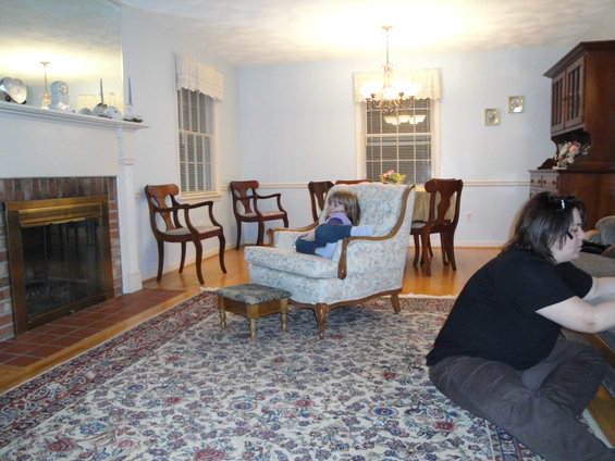 Interior of a living room with a fireplace, chairs, a child in an armchair, and a woman on the floor