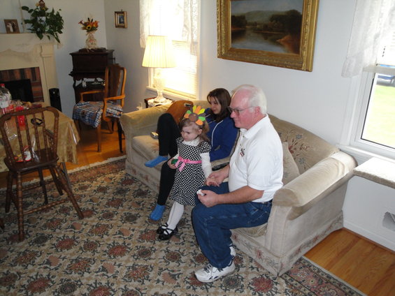 Family gathered in a living room, with a man, two girls, and a toddler on a sofa