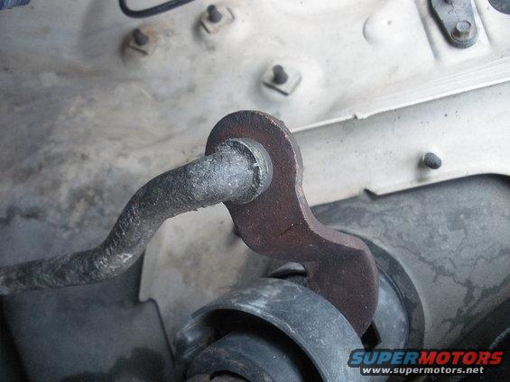 Close-up of rusty metal linkage connected to a black rubber bushing, likely part of a steering column