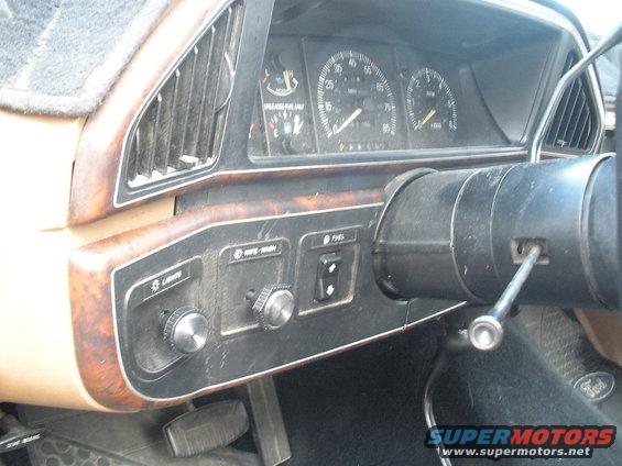 Dashboard with wood grain trim, gauges, and steering column. The 1990 Ford Bronco interior is dusty