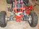 1987 Honda 250 R - Close-up view of the front suspension system of an ATV, showing the red frame and dual shock absorbers.