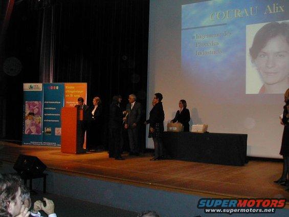 People on stage at an event with a projector screen showing a name and photo