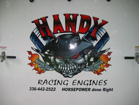 White trailer door with a graphic of a skull wearing a Ford hat, surrounded by pistons and flames, with text 'HANDY RACING ENGINES'