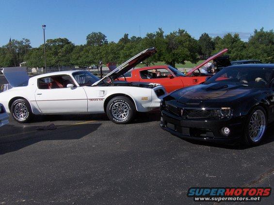 1977 Pontiac Trans Am, red Trans Am, and black modern Trans Am parked outside with hoods open