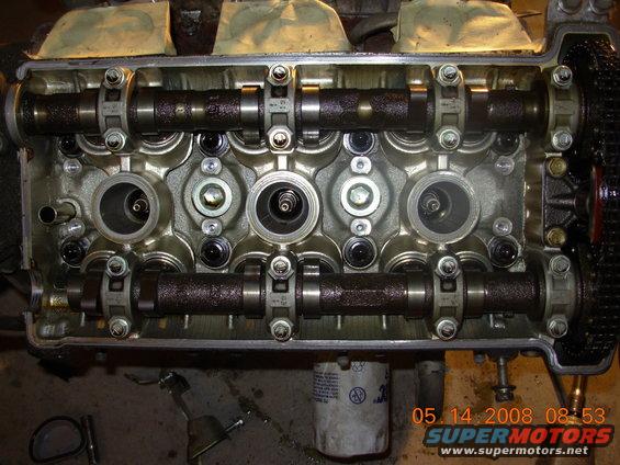 Engine cylinder head removed, showing camshafts, valves, and spark plug holes. Oil filter visible below
