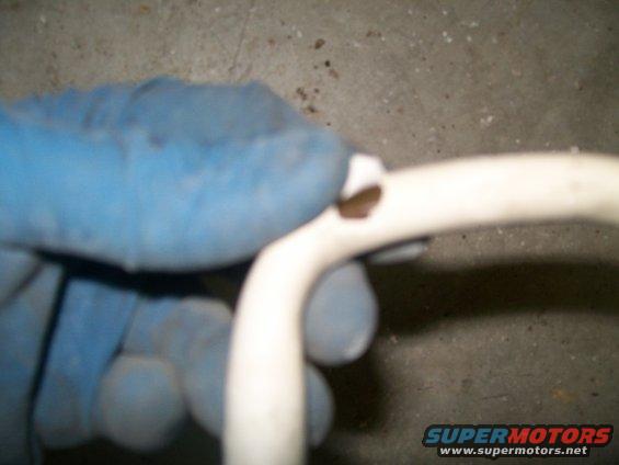 Gloved hand holding a white plastic tube with a hole in it. Supermotors.net logo visible