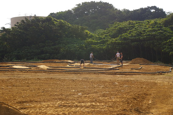 Dirt track with black tubing borders and piles of sand, with four people working