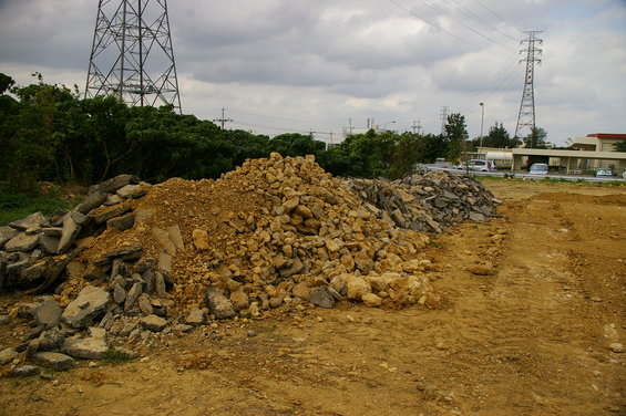 piles of rubble and dirt in a construction area with power lines and trees in background