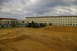 1986 Ford Bronco - A construction site with multiple buildings and various vehicles, including heavy machinery and a military truck, under a cloudy sky.