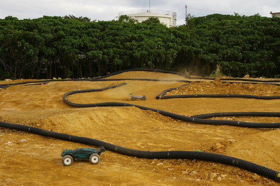 Two remote control cars race on a dirt track with black tubing borders