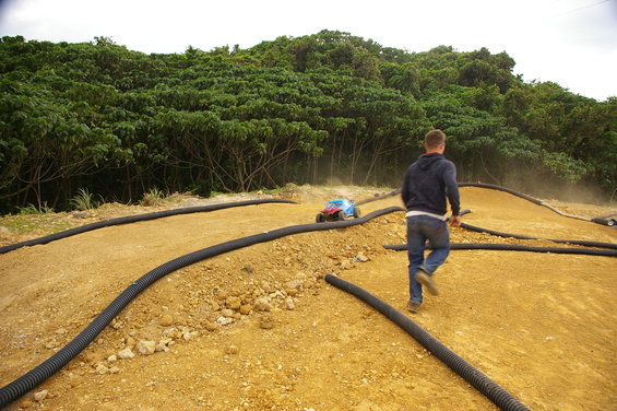 Blue remote control car on dirt track with man walking