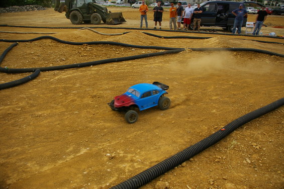 Blue and red radio-controlled car on a dirt track with black tubing