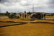 1986 Ford Bronco - Men gather around a dirt track to watch remote control cars race, with a backhoe and van nearby.