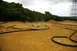 1986 Ford Bronco - RC cars race on a dusty dirt track with tubing borders and trees in the background.