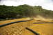 1986 Ford Bronco - A remote control car races on a dusty track bordered by black tubing and lush green trees.