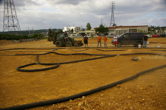 RC car kicking up dust on a dirt track, with people and a van nearby